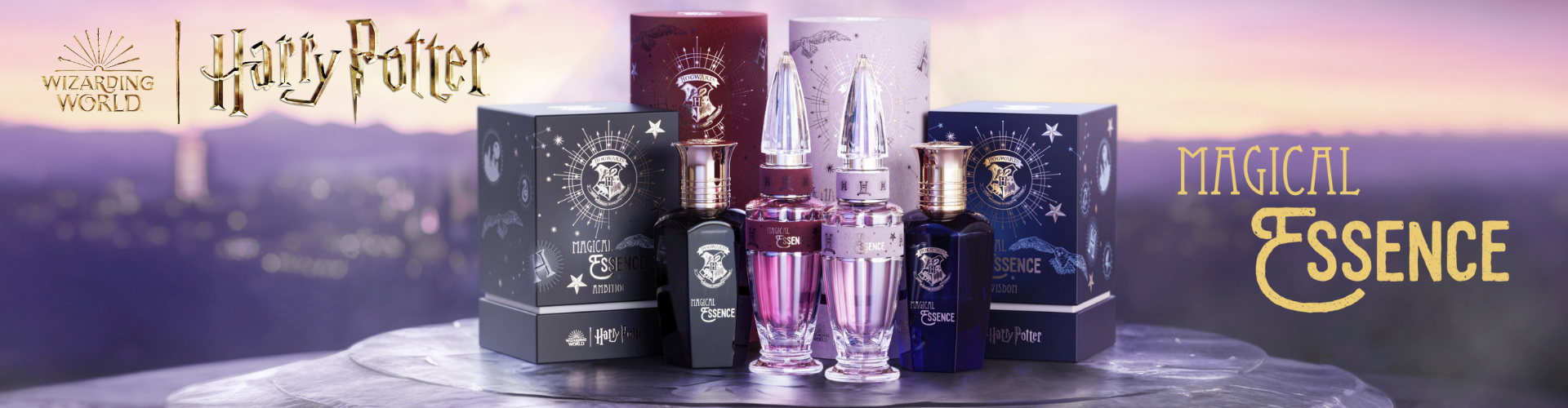 Werbebanner zur Magical Essence Parfumkollektion aus der Wizarding World. Vier Flakons in Schwarz, Rot, Rosa und Blau stehen zwischen farblich abgestimmten Verpackungen mit magischen Symbolen. Links das Harry-Potter- und Wizarding-World-Logo, rechts der goldene Schriftzug „Magical Essence“. Der Hintergrund zeigt eine verzauberte Landschaft in Pastellfarben.